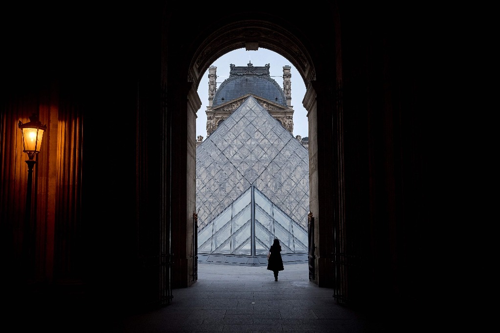 París. Un peatón camina por el museo del Louvre mientras al fondo se contempla su pirámide, diseñada por el arquitecto chino-estadunidense Ieoh Ming Pei, en la capital francesa. Foto Afp / Kiran Ridley