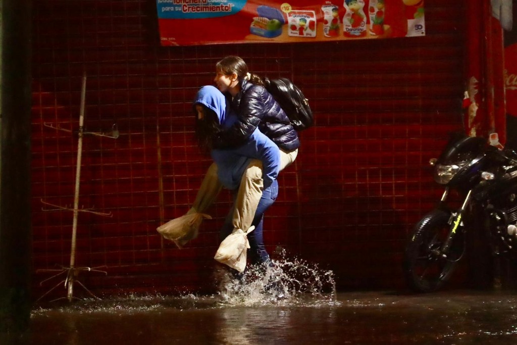 Dos mujeres se ayudan a cruzar una calle inundada por las fuertes lluvias en la  alcaldía de Tlalpan. Foto: Luis Castillo