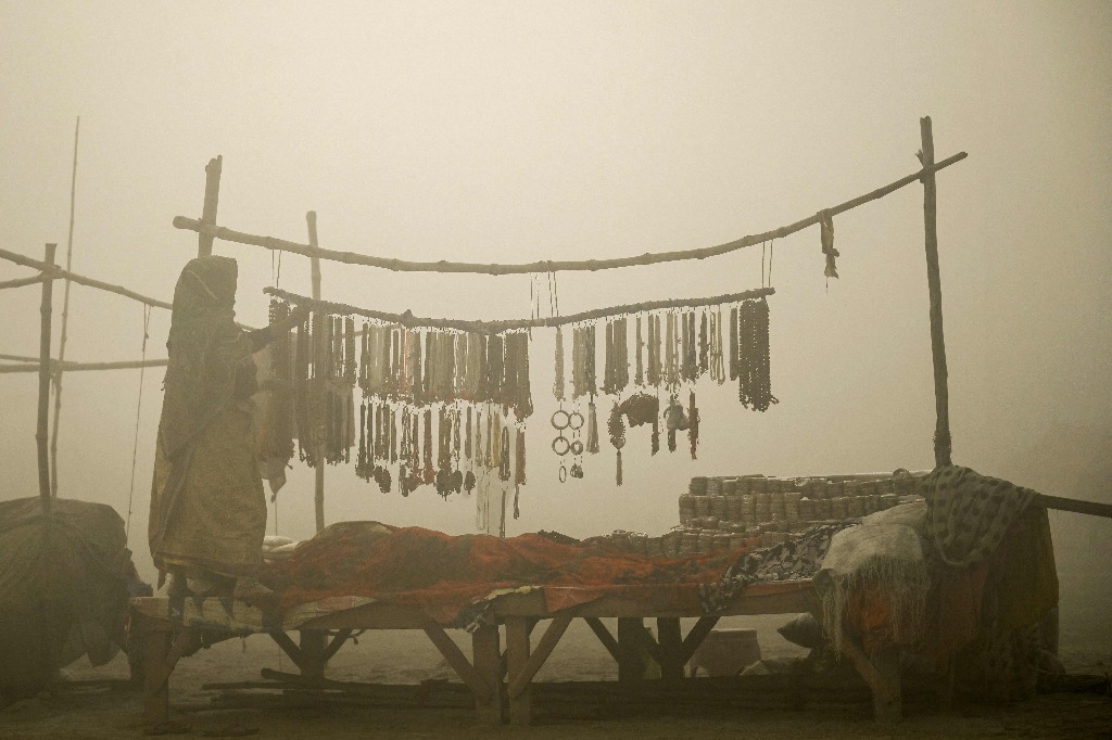 Prayagraj. Una vendedora organiza sus mercancías después de abrir su puesto en una mañana fría y brumosa cerca de Sangam, la confluencia de los ríos Ganges, Yamuna y el mítico Saraswati, antes del festival Maha Kumbh Mela en esta población india. Foto Afp / Money Sharma